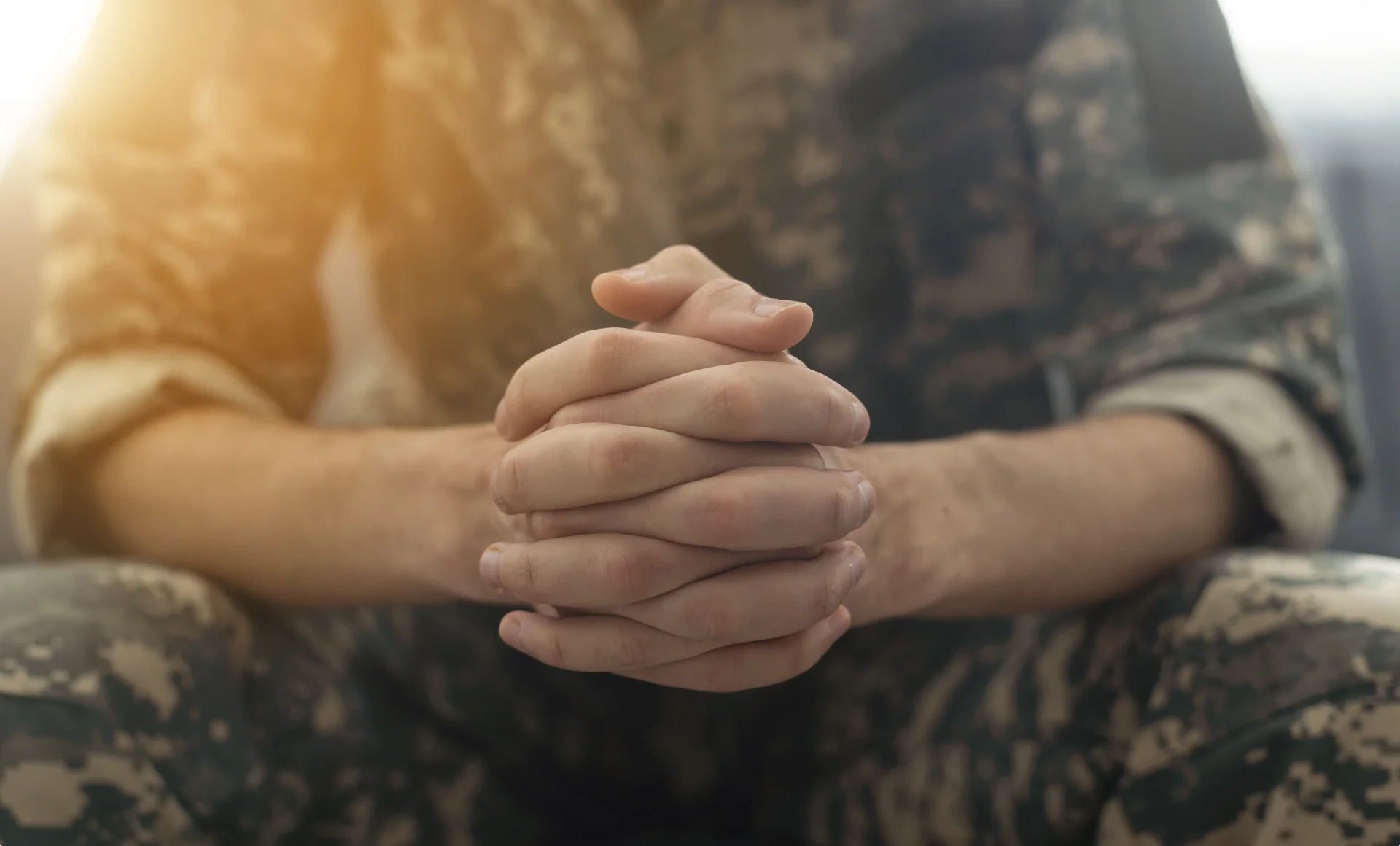 Close-up of clasped hands of a person in military camouflage uniform